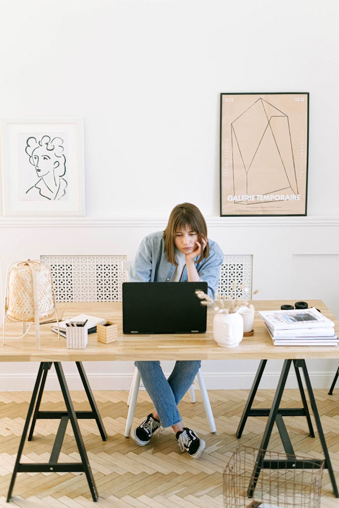 Focused woman using a laptop at a chic home office desk with stylish decor.